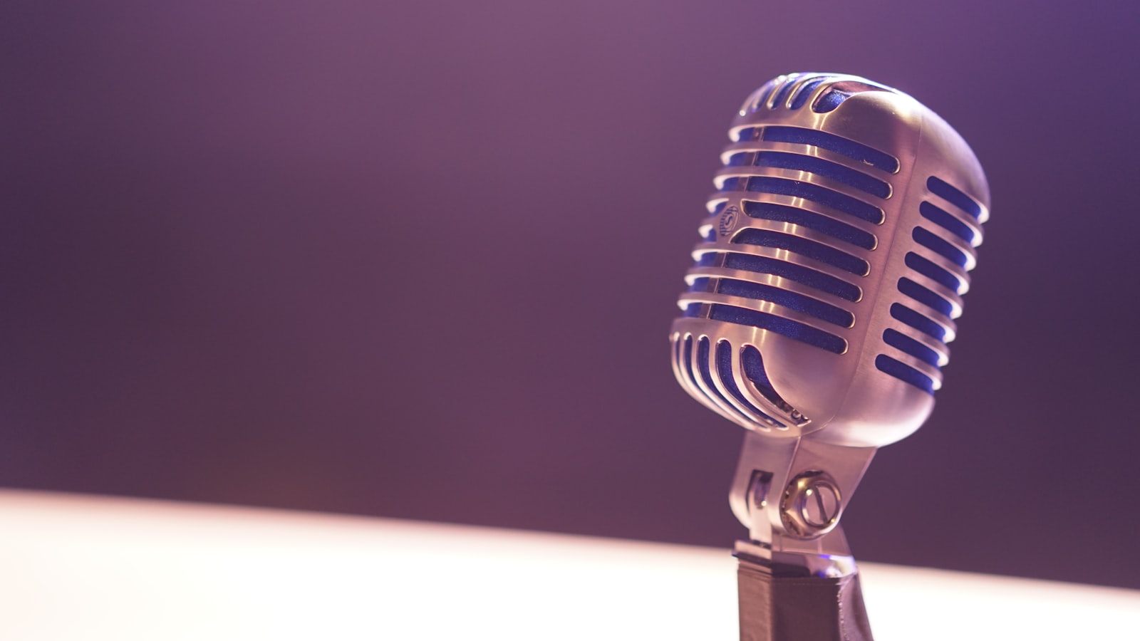 Professional microphone in a recording studio with soundproofing panels and a computer screen showing audio waveforms