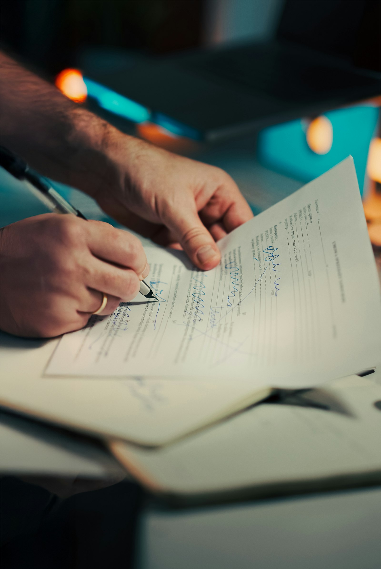 Person signing a printed contract document with a pen on a desk
